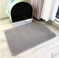 Tapis de litière pour chat double couche gris devant un bac à litière.